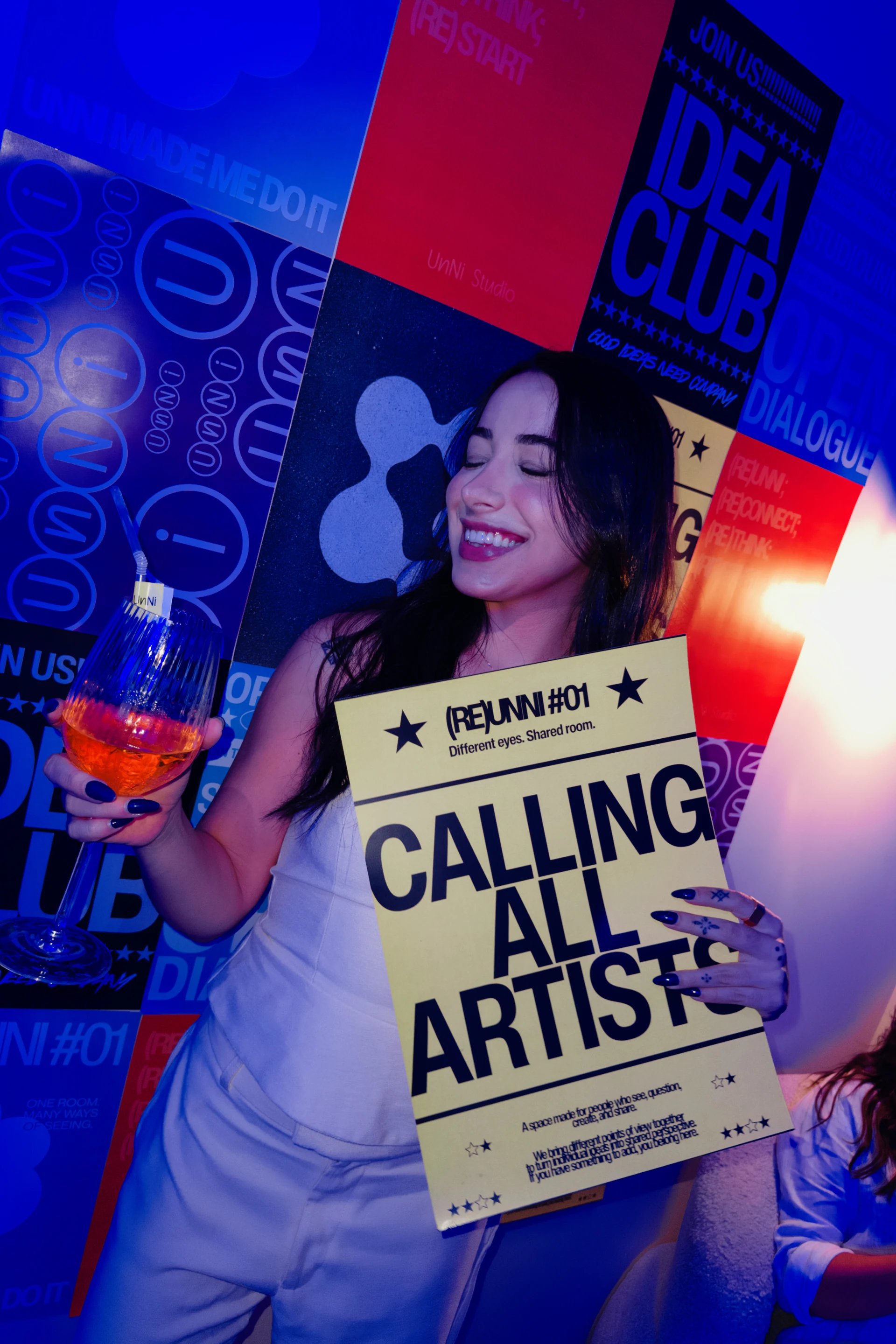 Participante com cartaz Calling All Artists sob a luz azul do encontro